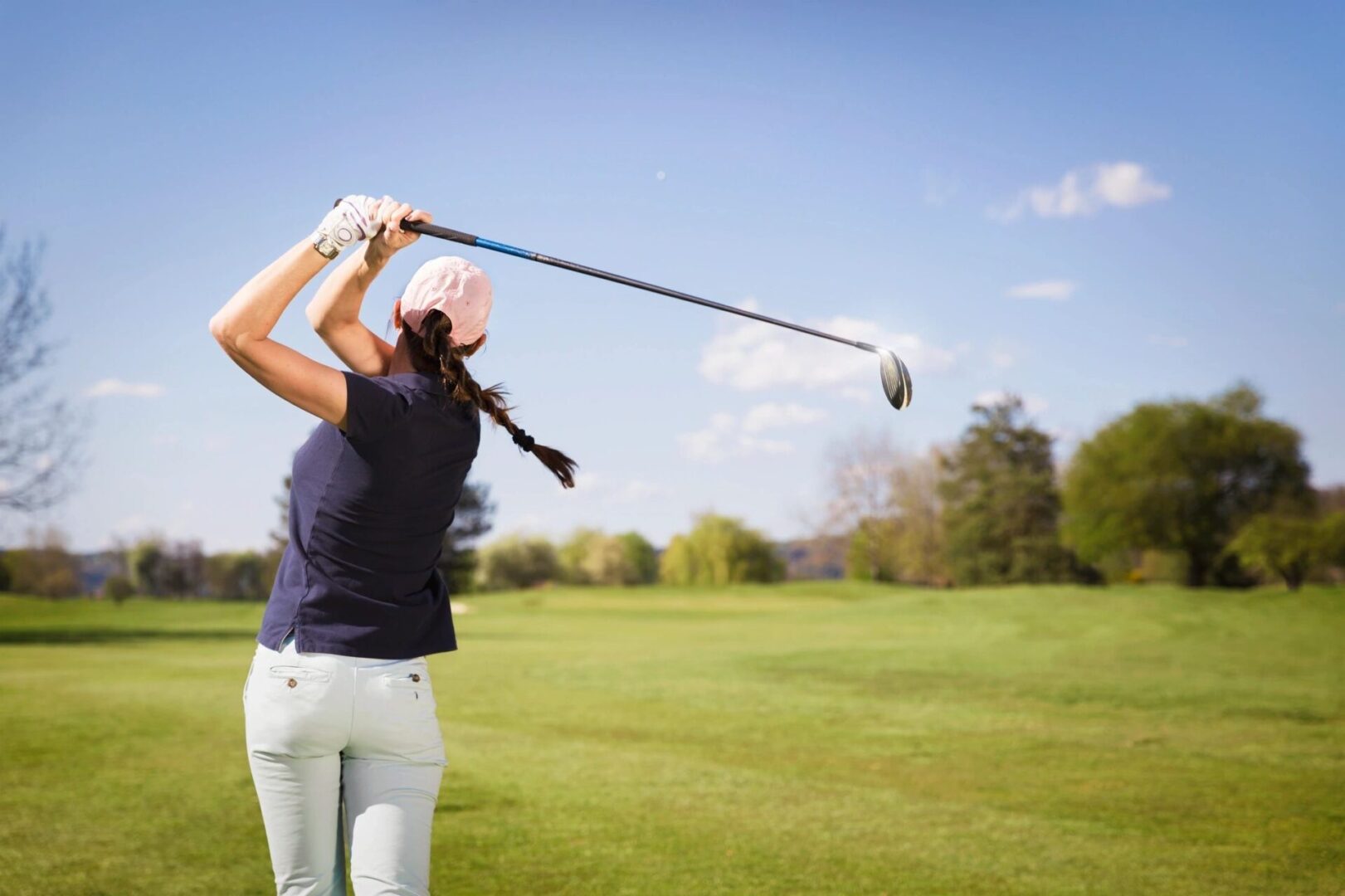 A woman swinging at a golf ball on the course.